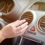 Driver hand tuning air ventilation grille, emergency flasher switch and light in modern car interior