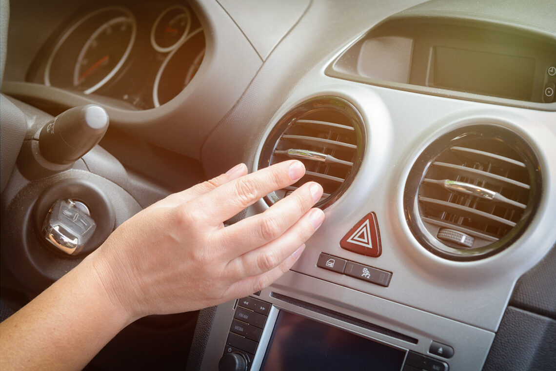 Driver hand tuning air ventilation grille, emergency flasher switch and light in modern car interior